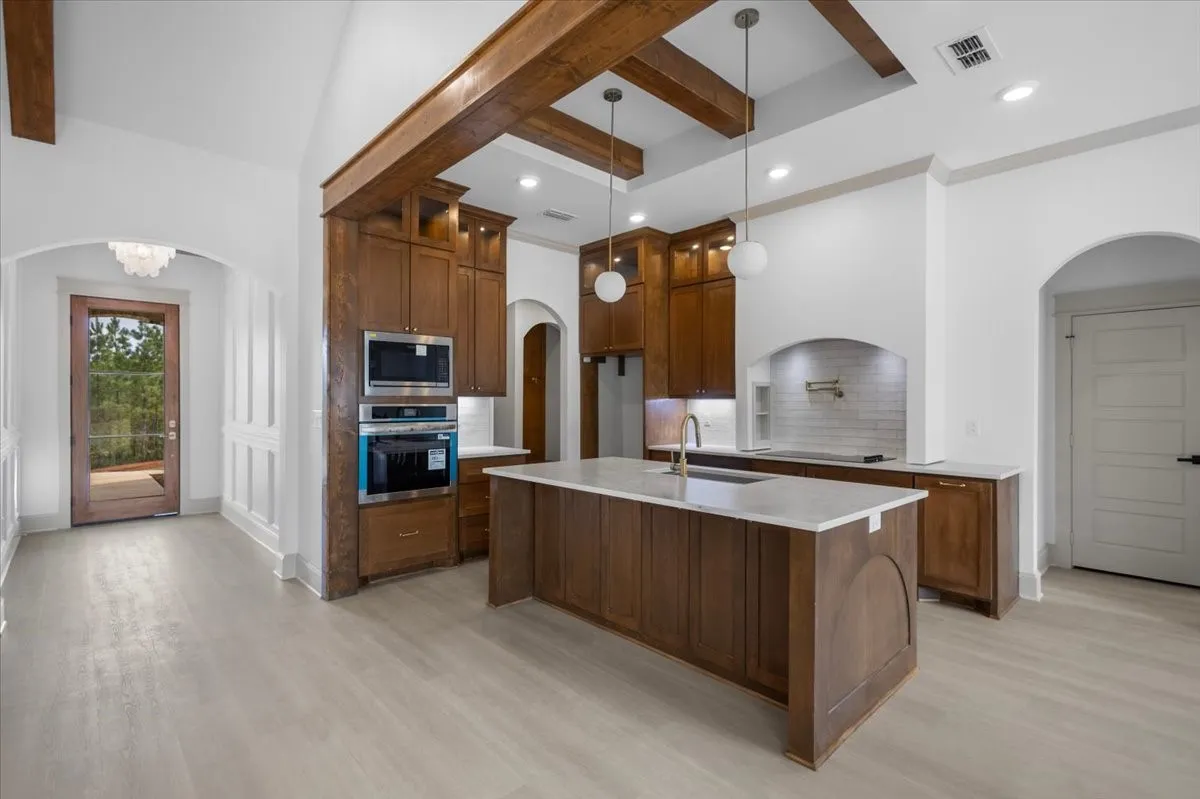 Gourmet kitchen featuring wood cabinetry, integrated stainless steel appliances, a center island with a sink, and a tile backsplash