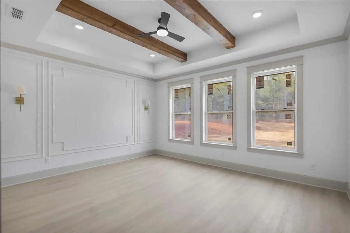 Tray ceiling with exposed wood beams, recessed lighting, decorative wall molding, three windows, and wood-finish flooring