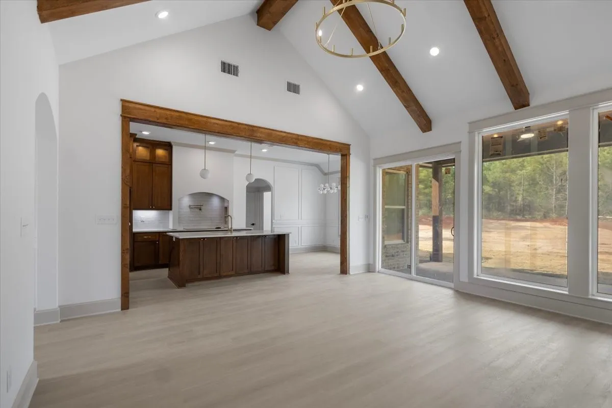 Vaulted ceiling with exposed wood beams, wood-finish flooring, recessed lighting, and a large sliding glass door