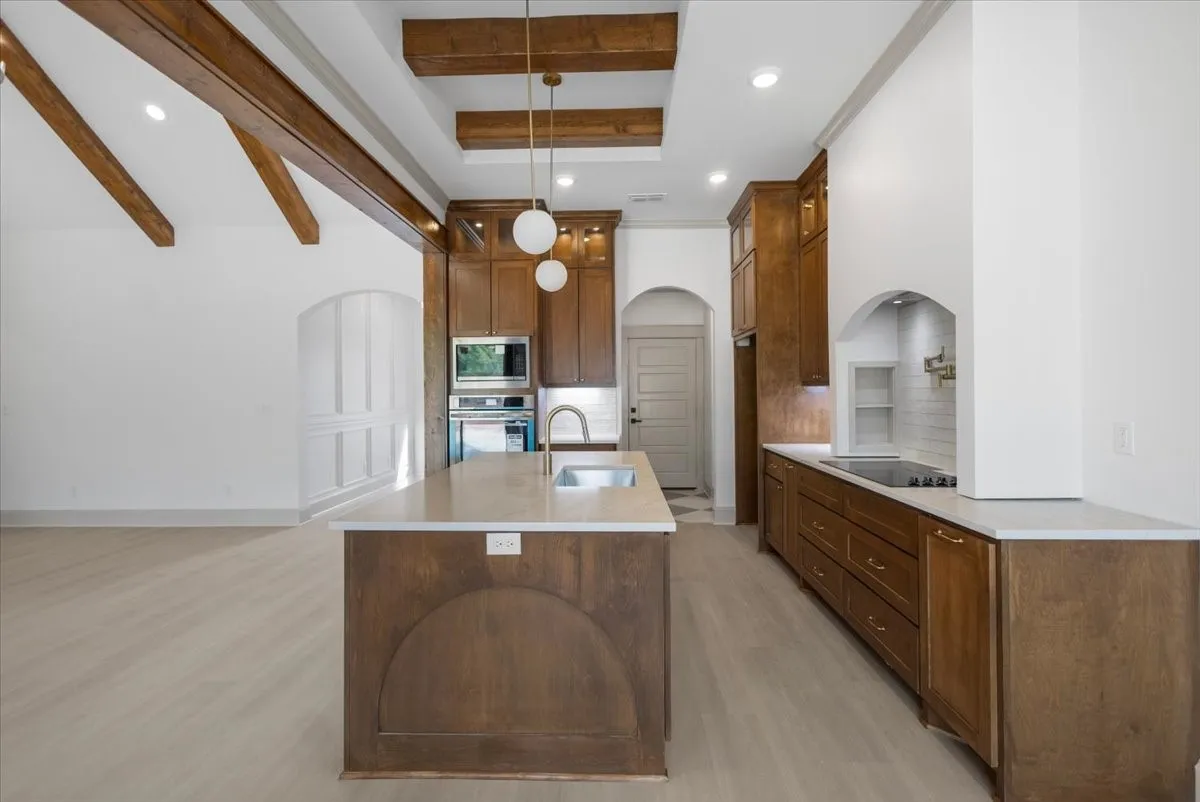 Open-concept kitchen with vaulted ceiling, exposed wood beams, a spacious center island with an undermount sink, and stainless steel appliances