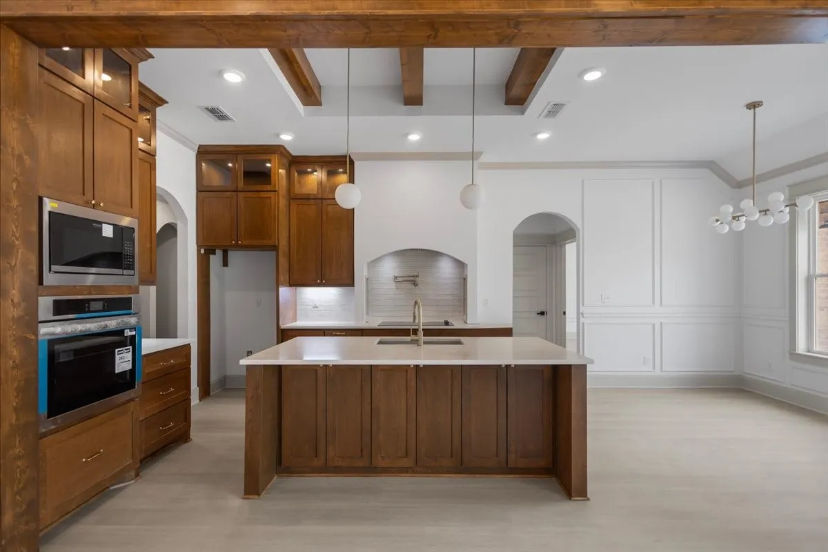 Exposed wood beams, recessed lighting, integrated stainless steel appliances, central island with countertop, and decorative wall paneling