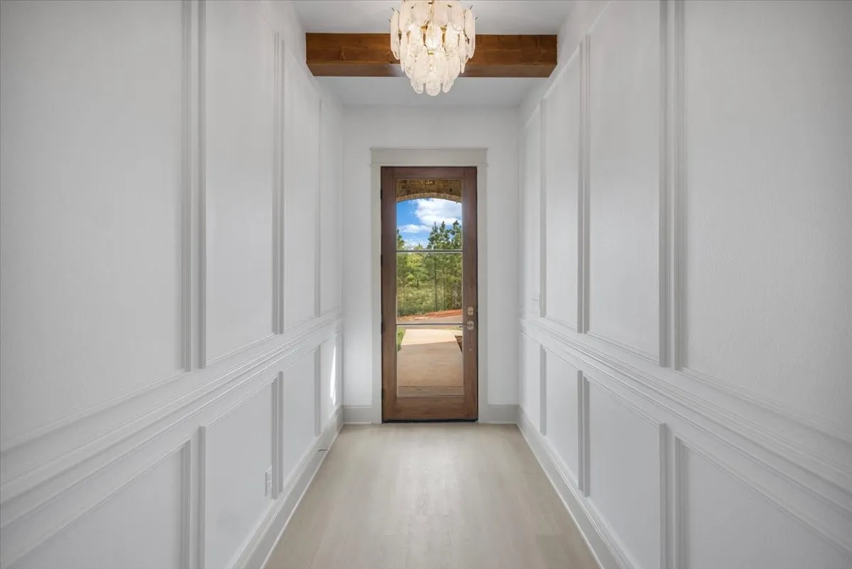 Hallway with decorative wainscoting, wood-finish flooring, exposed wood beam, and a glass-paneled entry door