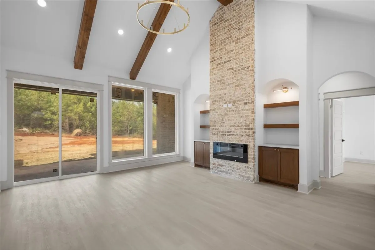 Vaulted ceiling with exposed wood beams, brick fireplace with integrated insert, built-in shelving and cabinetry, recessed lighting, and wood-finish flooring