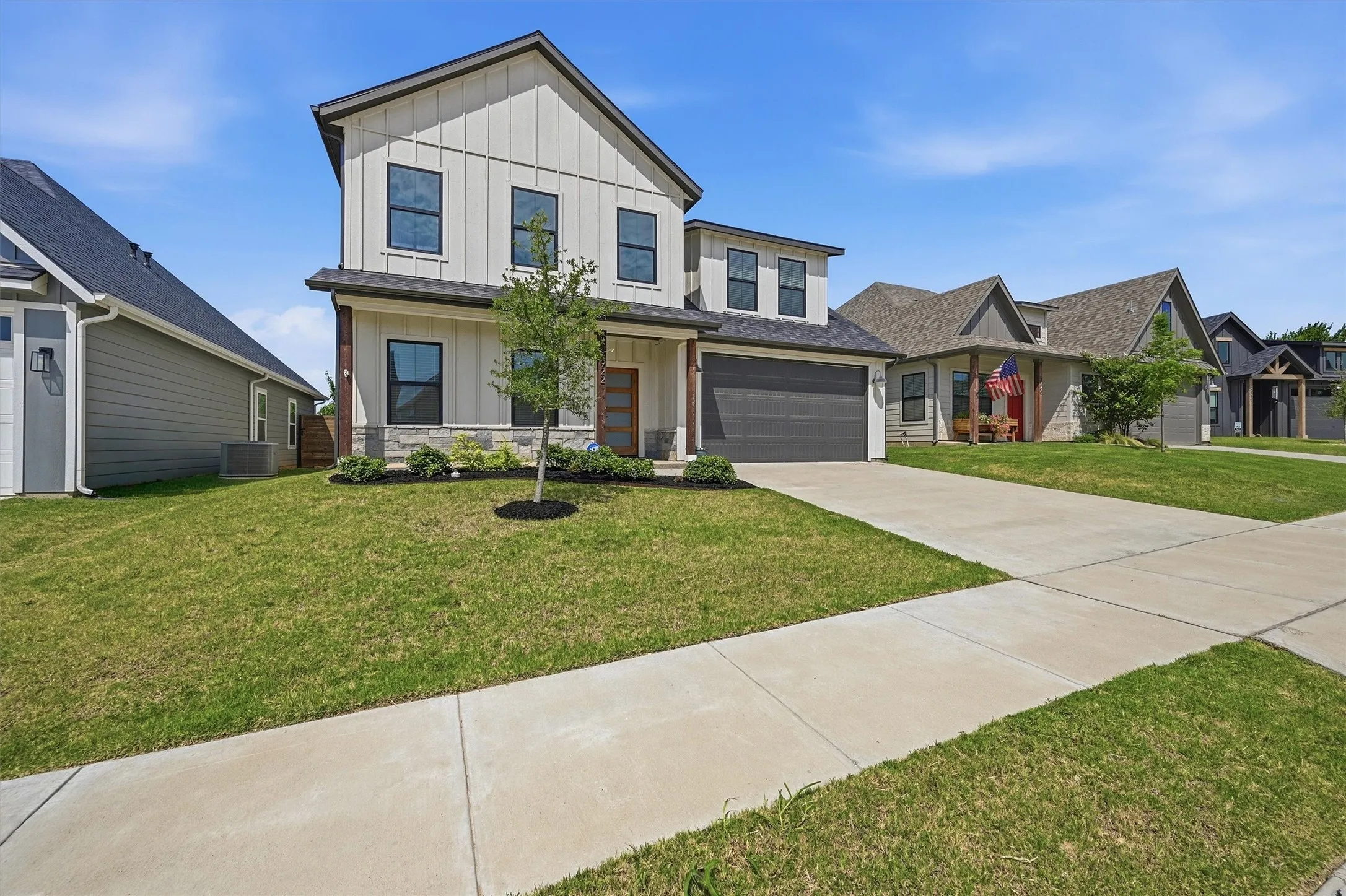 Two-story residence featuring vertical siding, stone accents, a dark-toned garage door, and a concrete driveway