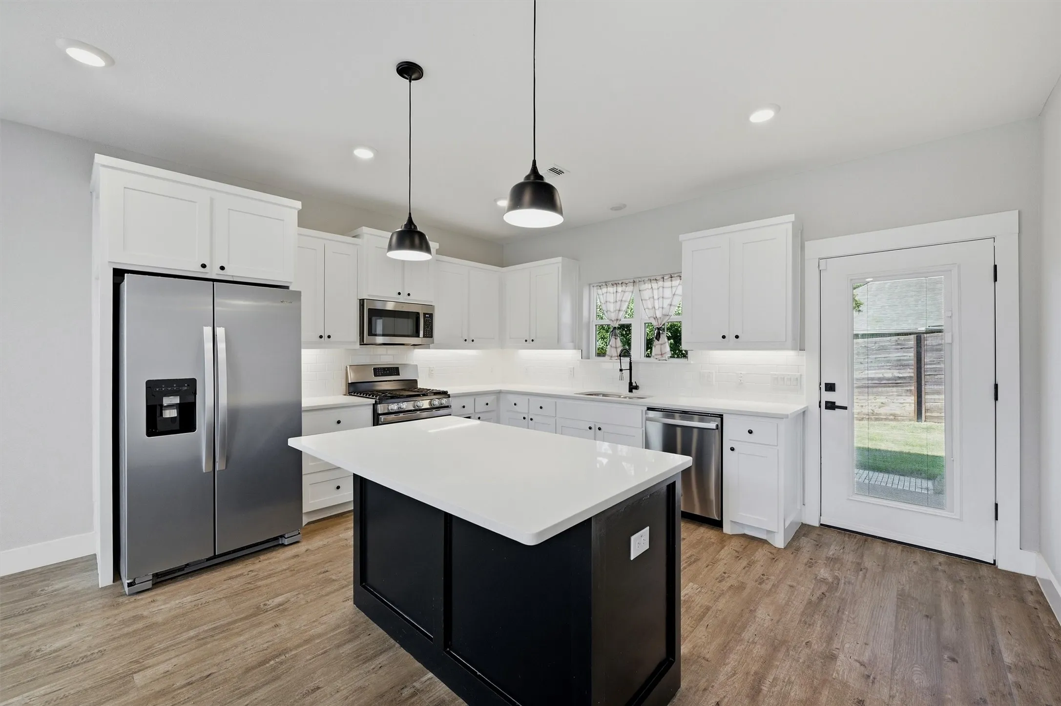 Kitchen featuring white shaker cabinetry, stainless steel appliances, a center island with a light-toned countertop, and wood-finish flooring