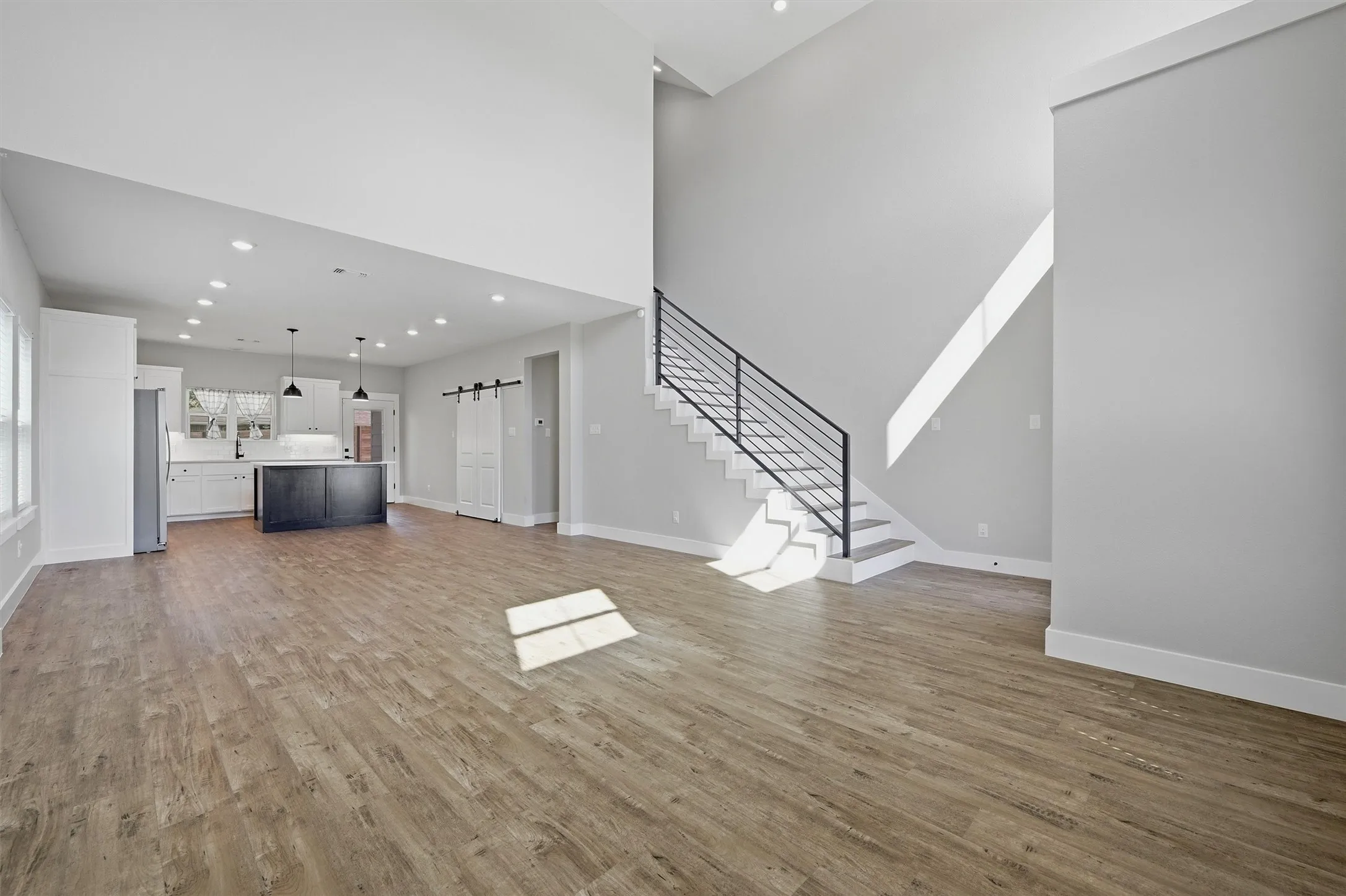 Expansive living area featuring high ceilings, wood-finish flooring, and a modern black metal staircase railing