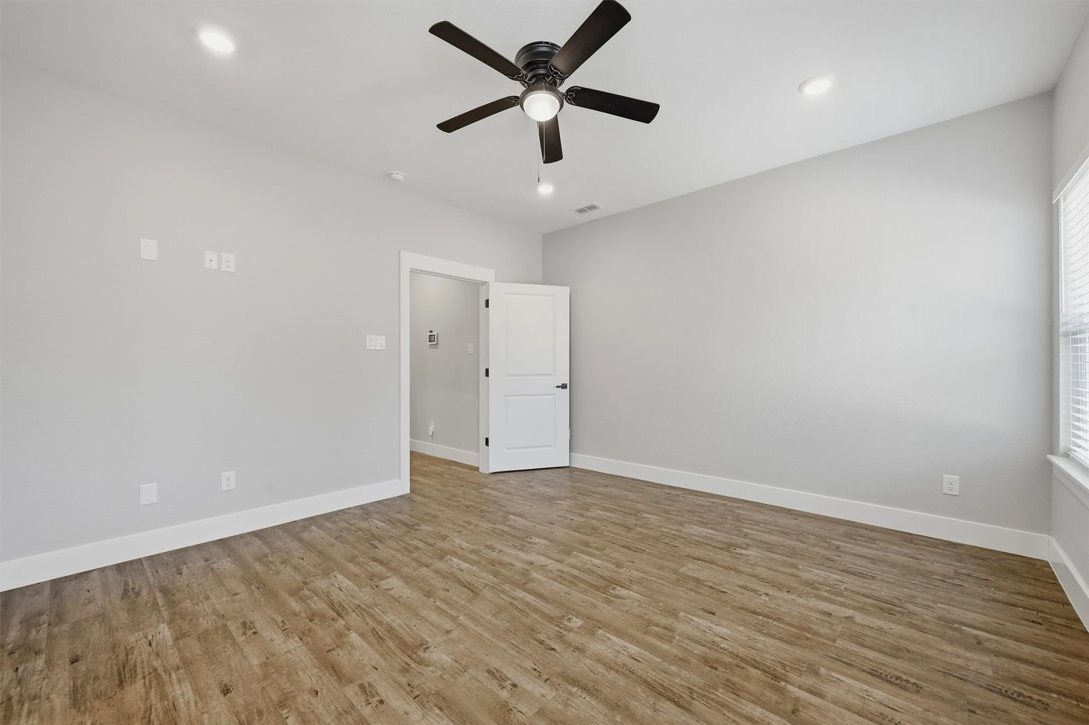 Wood-finish flooring, recessed lighting, ceiling fan with light, white interior door, and window with blinds