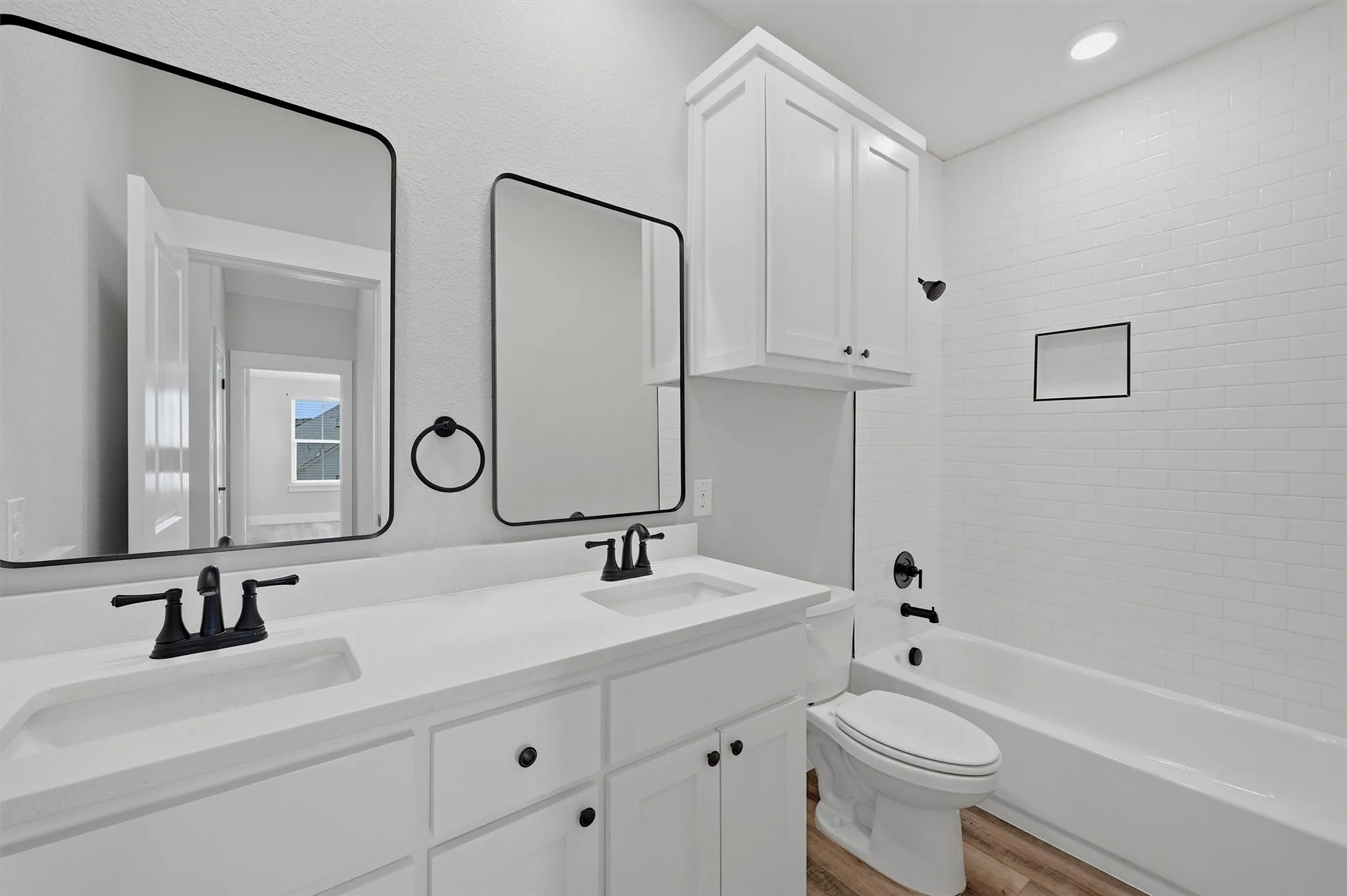 Double vanity with integrated sinks, matte black fixtures, built-in storage cabinetry, and white subway tile bath surround