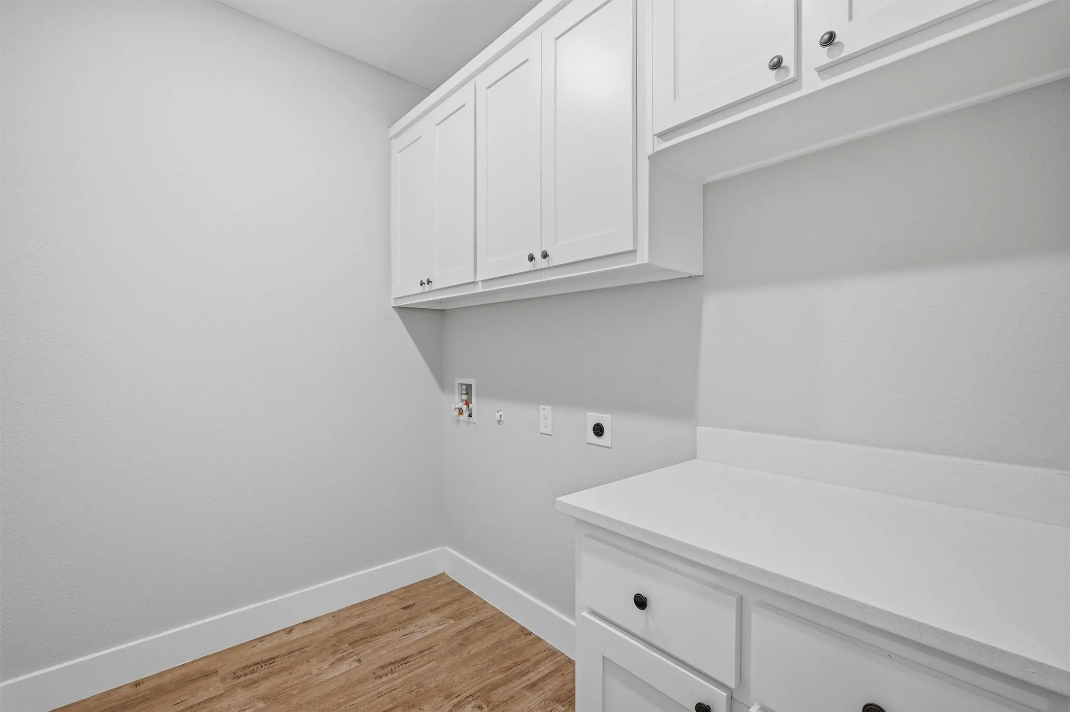 White cabinetry with black hardware, white countertops, and wood-finish flooring