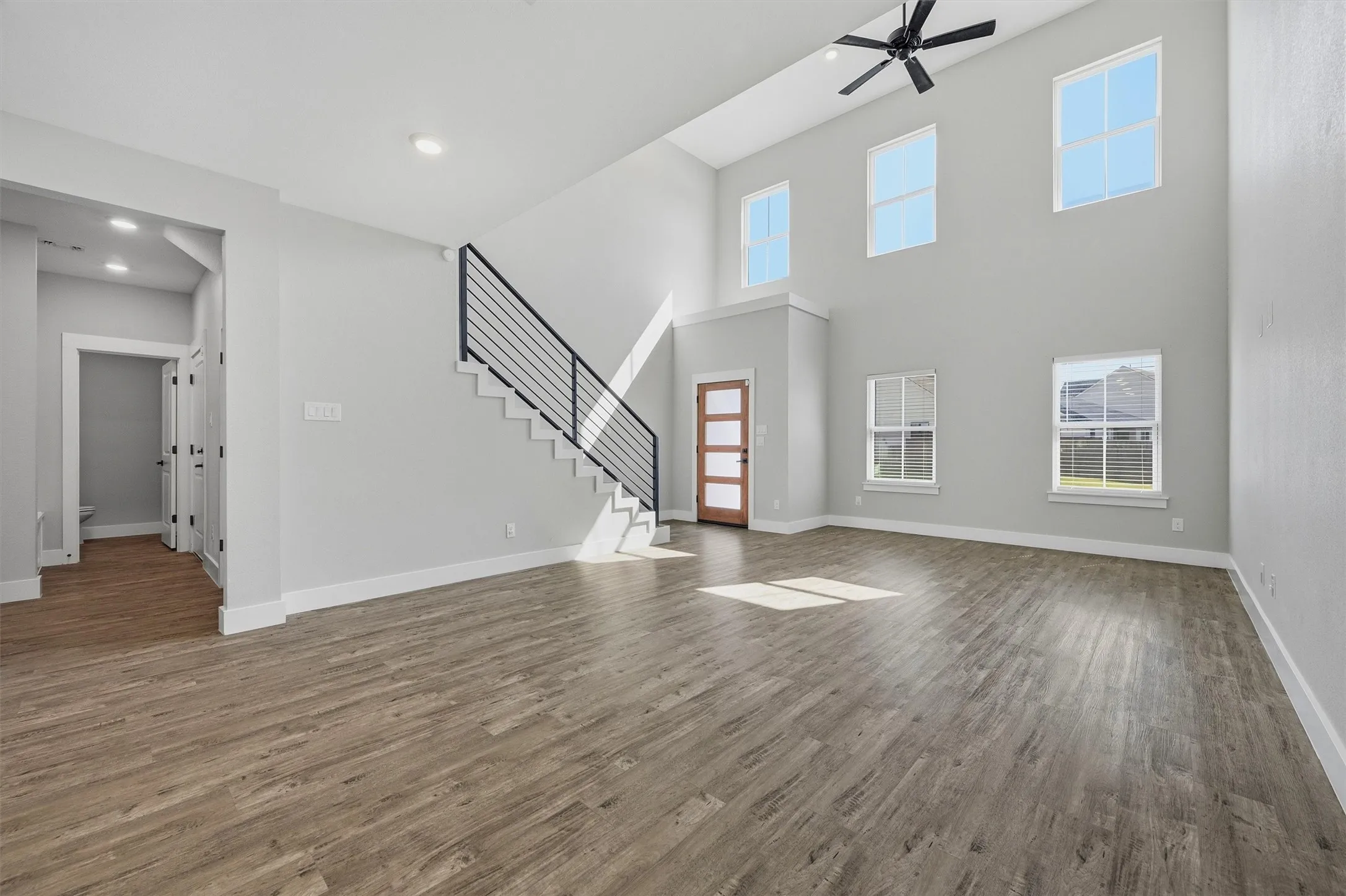 Expansive open-concept room featuring wood-finish flooring, a contemporary staircase with metal railing, and a vaulted ceiling