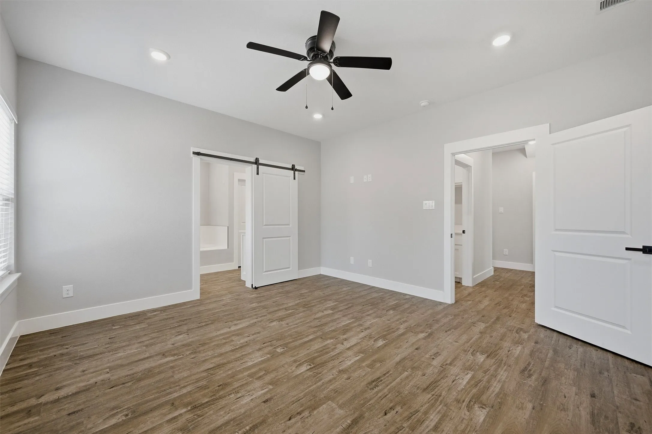 Vaulted ceiling, wood-finish flooring, recessed lighting, ceiling fan, and sliding barn door