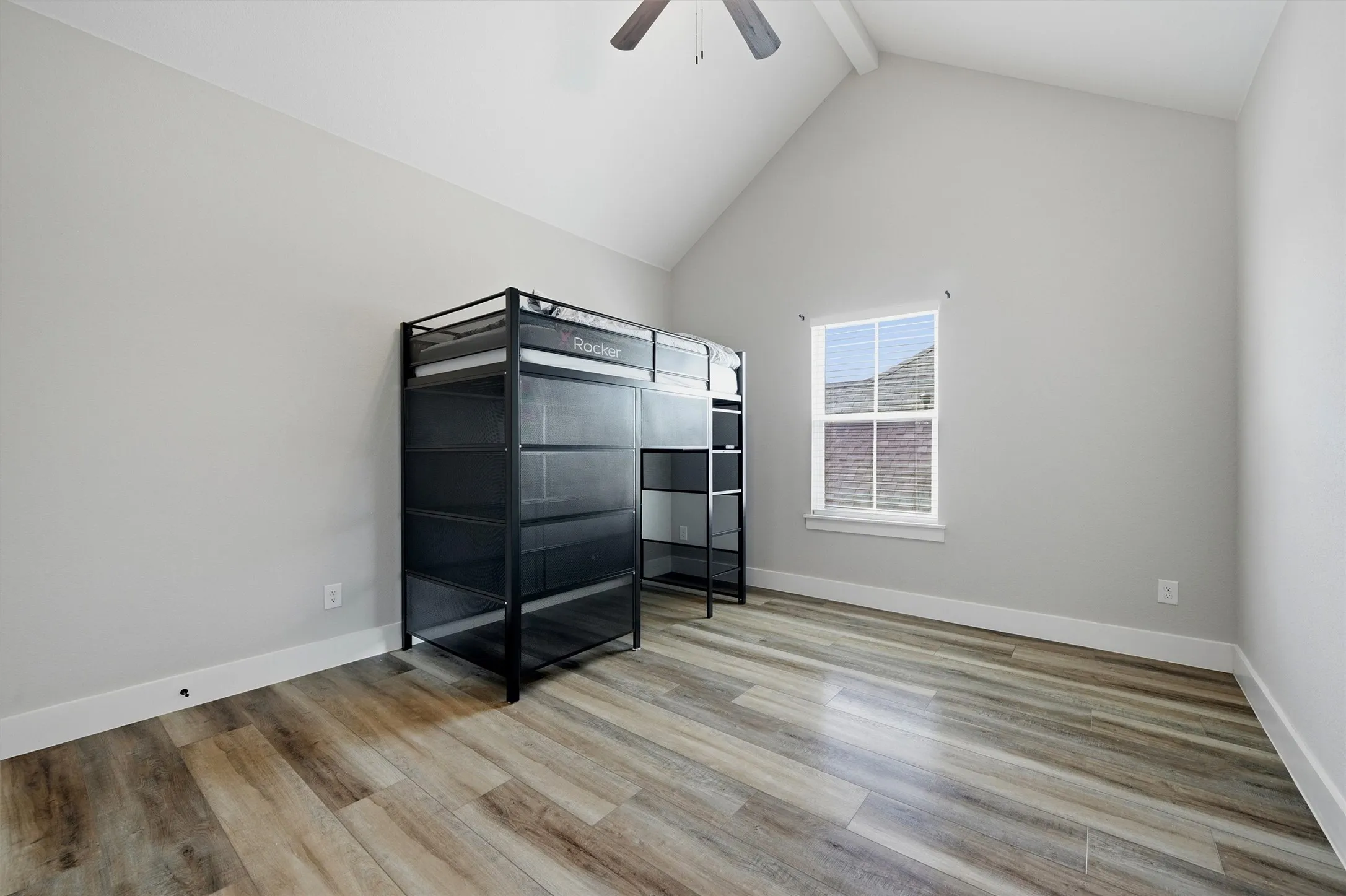 Vaulted ceiling with exposed beam, wood-finish flooring, and a window with blinds