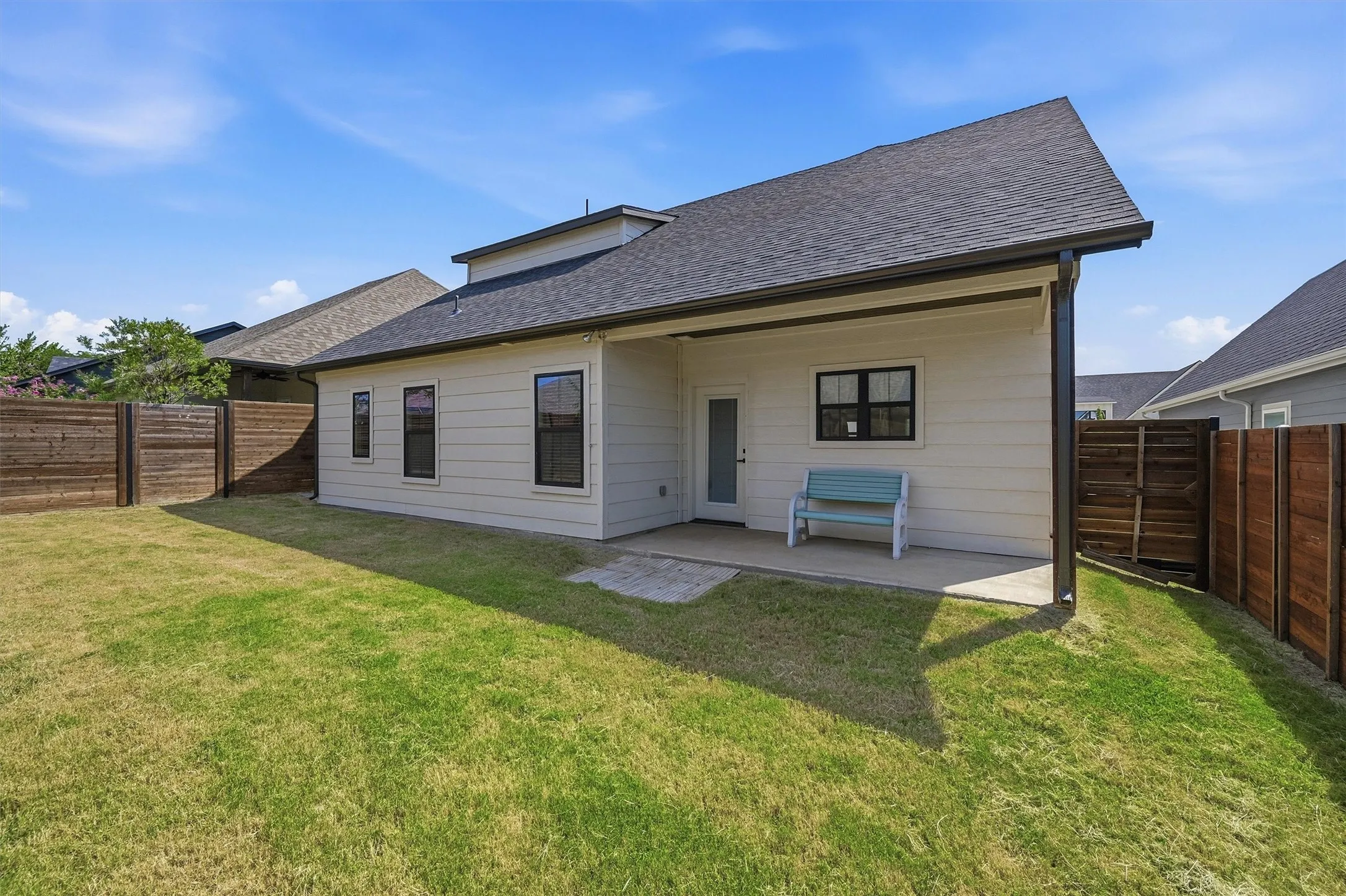 Expansive backyard featuring a manicured lawn, wood fencing, covered patio, and a shingled roofline