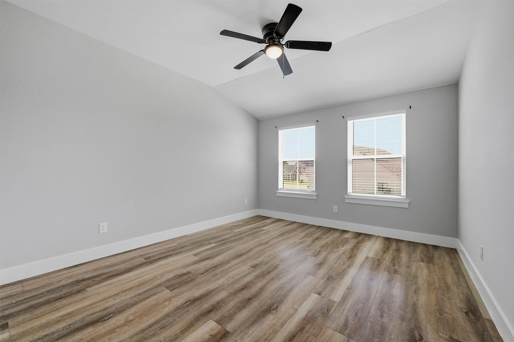 Vaulted ceiling with a ceiling fan, two windows with blinds, and wood-finish flooring