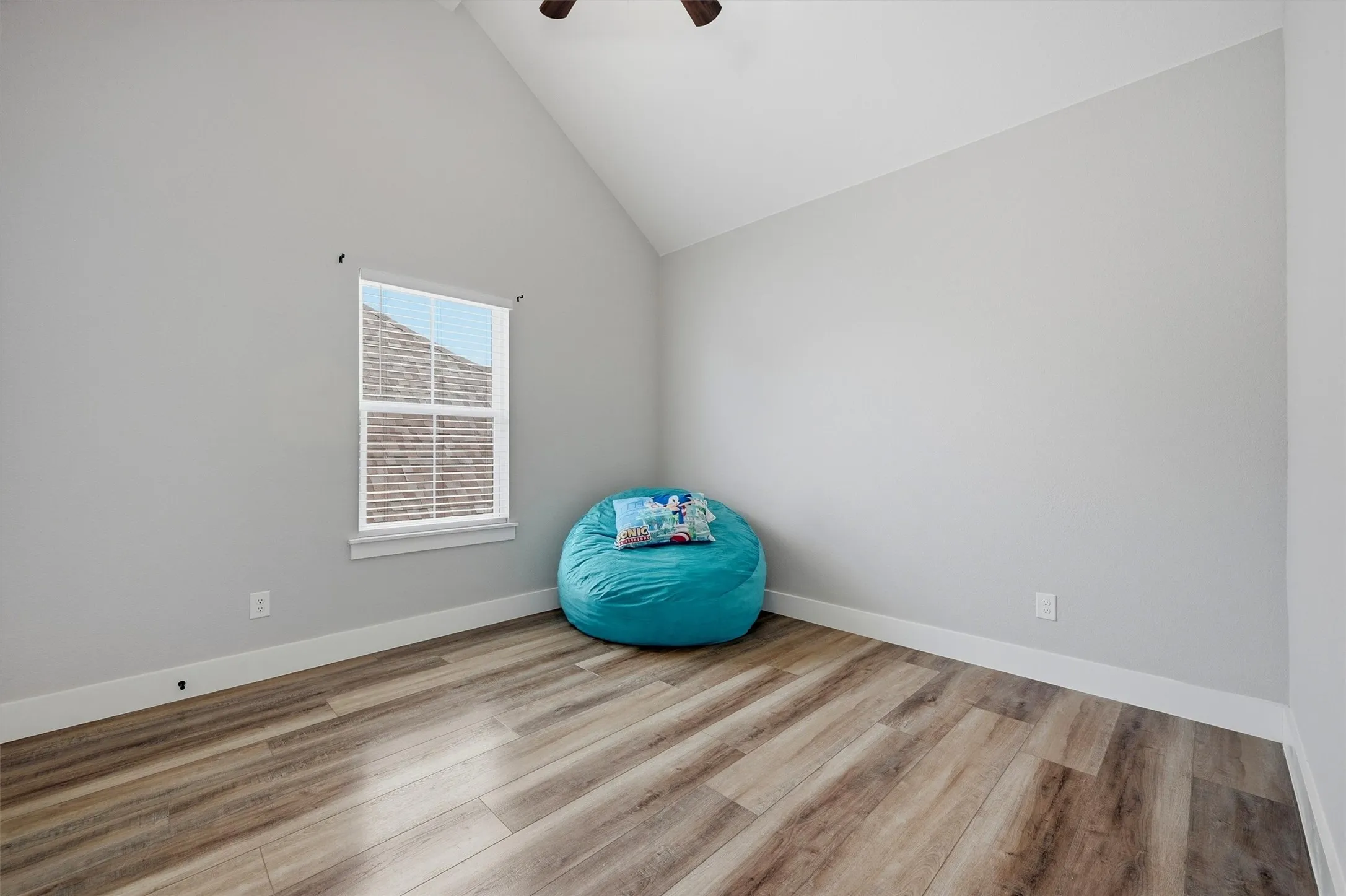 Vaulted ceiling, wood-finish flooring, white trim, and a window with natural light