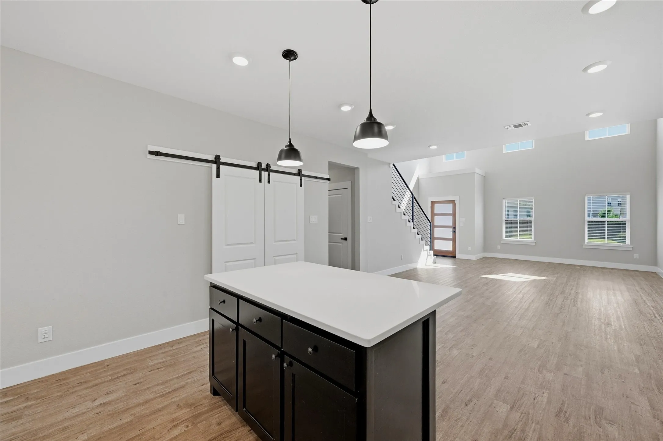 Kitchen island with white countertop, wood-finish flooring, two pendant lights, and a white barn door