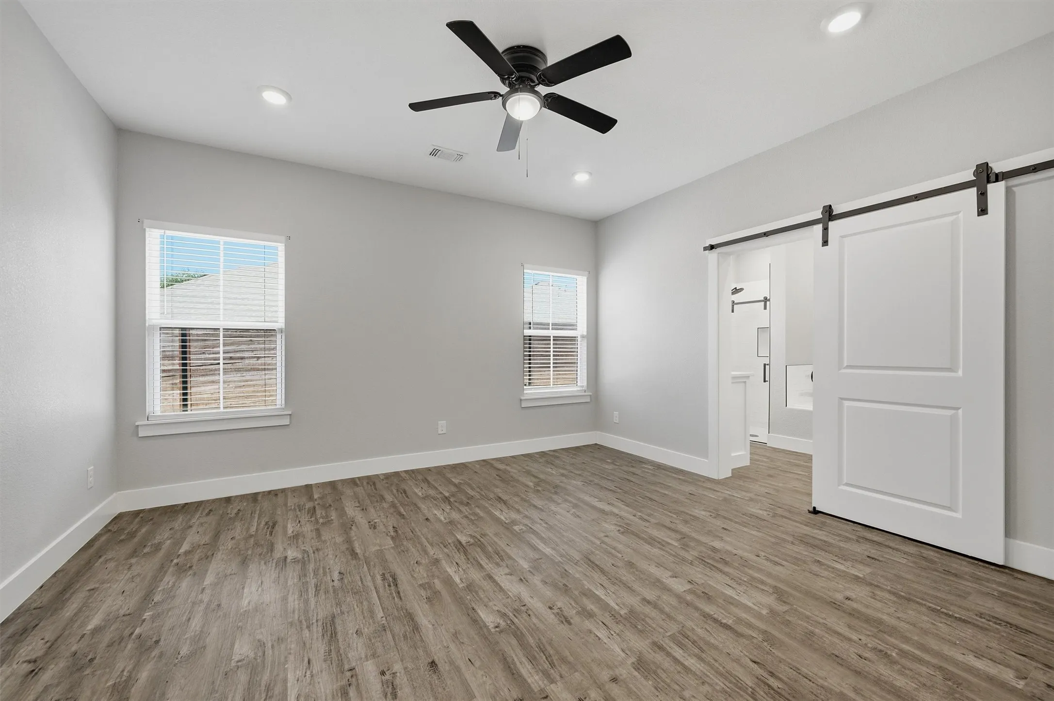 Spacious room featuring wood-finish flooring, two windows, recessed lighting, a ceiling fan, and a barn door entry