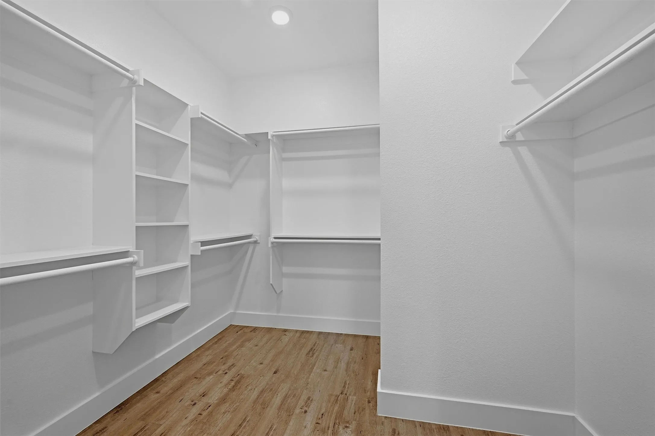 Walk-in closet featuring white built-in shelving, hanging rods, and wood-finish flooring