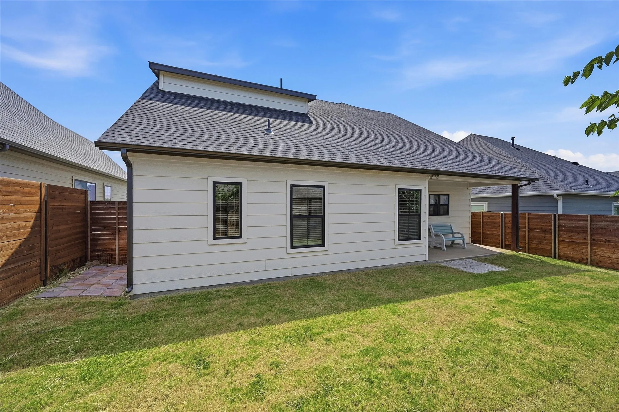 Exterior featuring light-colored siding, black-framed windows, a covered patio, and a privacy fence