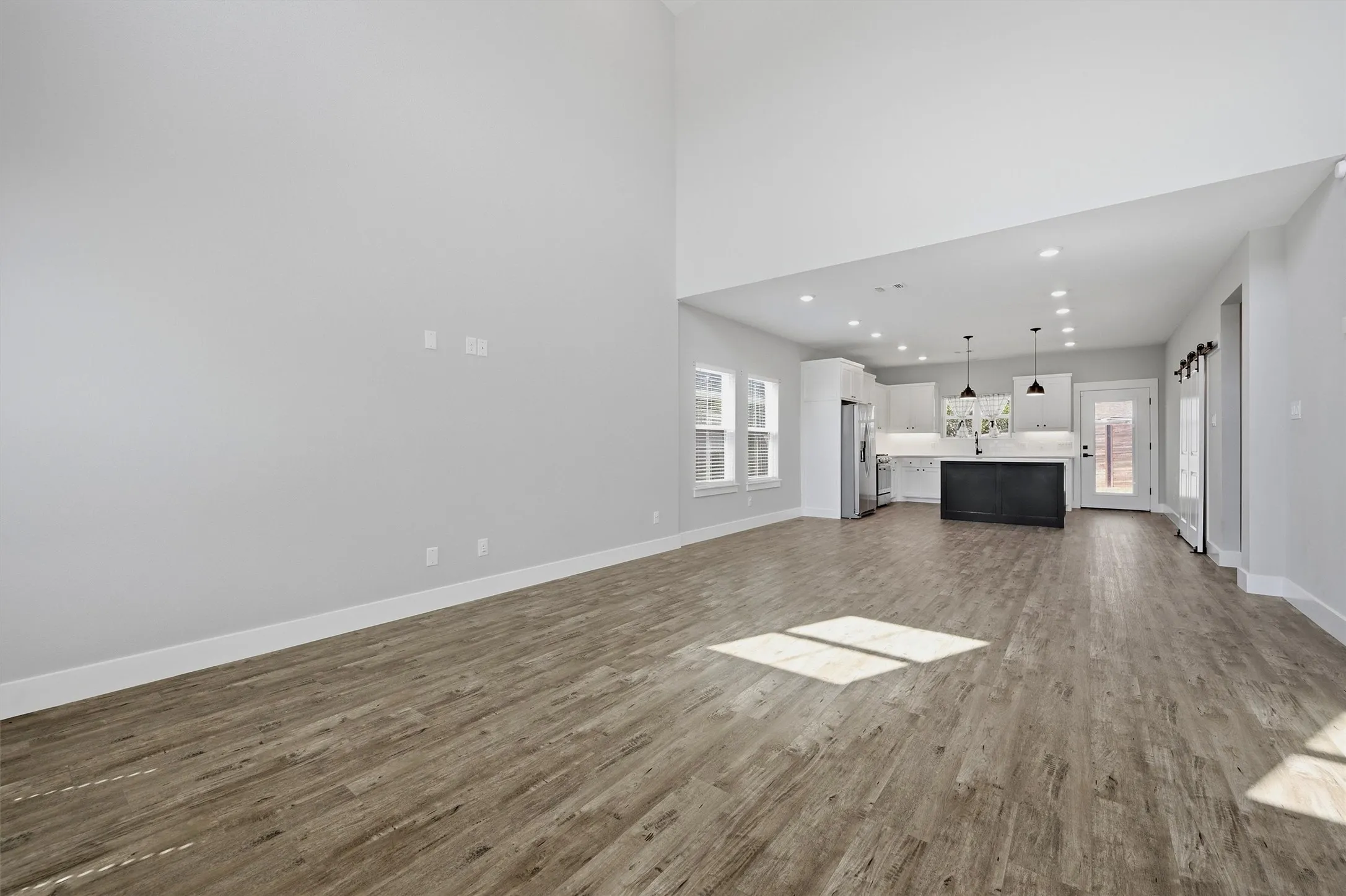 Vaulted ceiling, wood-finish flooring, white cabinetry, dark kitchen island, and recessed lighting