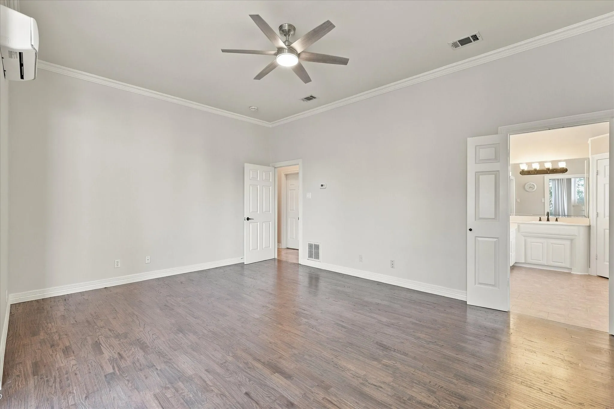 Spacious room featuring wood-finish flooring, crown molding, a ceiling fan, and an integrated mini-split unit