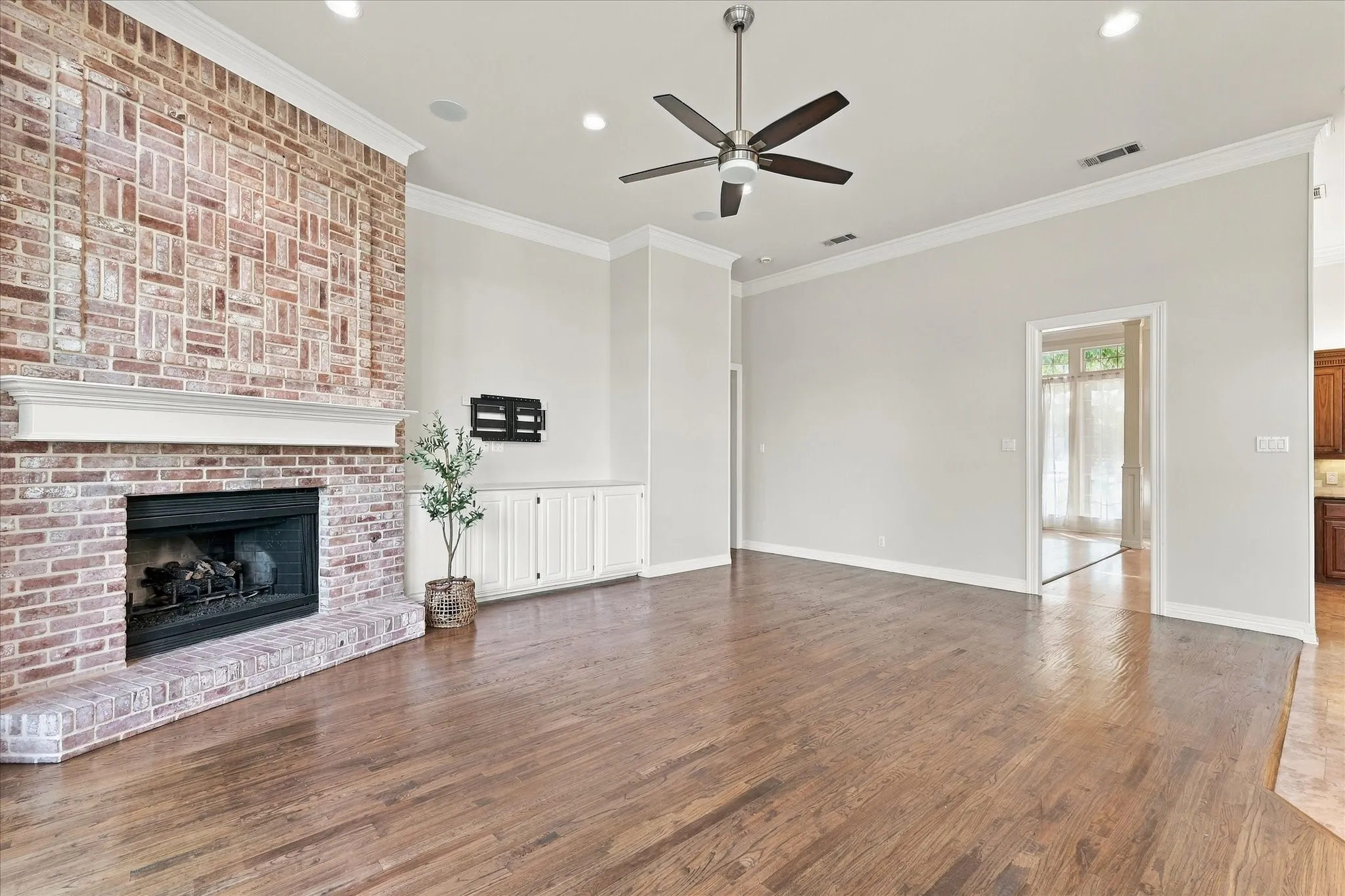 Wood-finish flooring, brick-clad fireplace with mantel, built-in cabinetry, recessed lighting, and ceiling fan