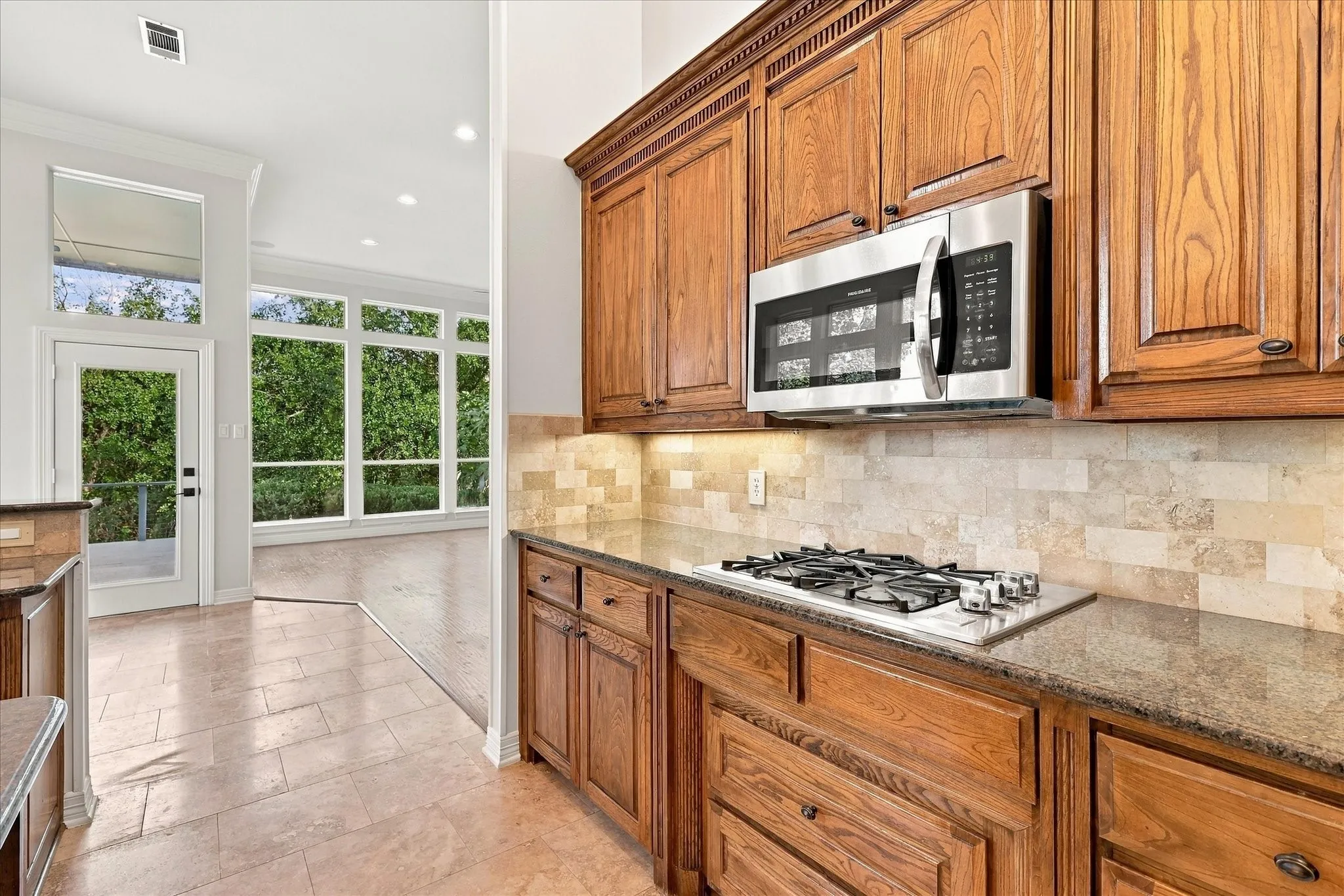 Recessed lighting illuminates wood cabinetry, stone-finish countertops, and a tiled backsplash