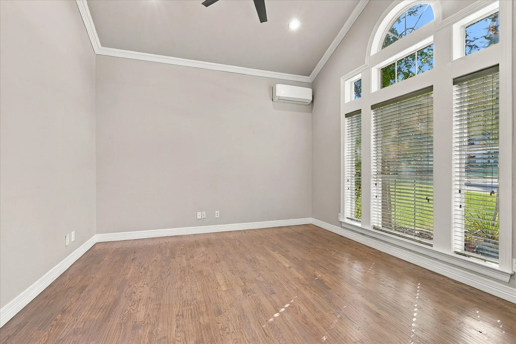 Vaulted ceiling, wood-finish flooring, architectural windows with an arched transom, crisp white trim, and a wall-mounted mini-split system