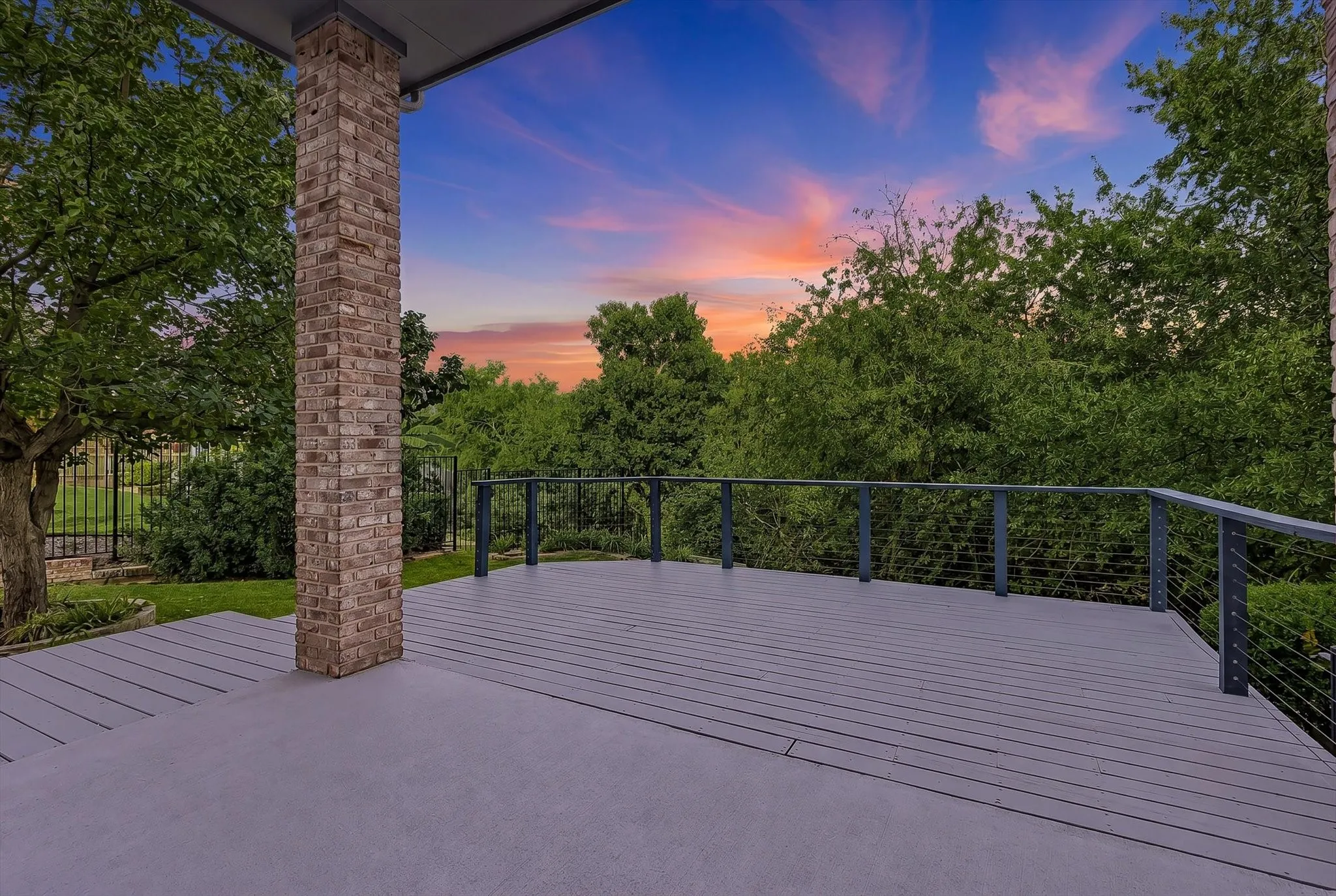 Expansive outdoor deck featuring wood-finish flooring, a contemporary cable railing system, and a brick support column