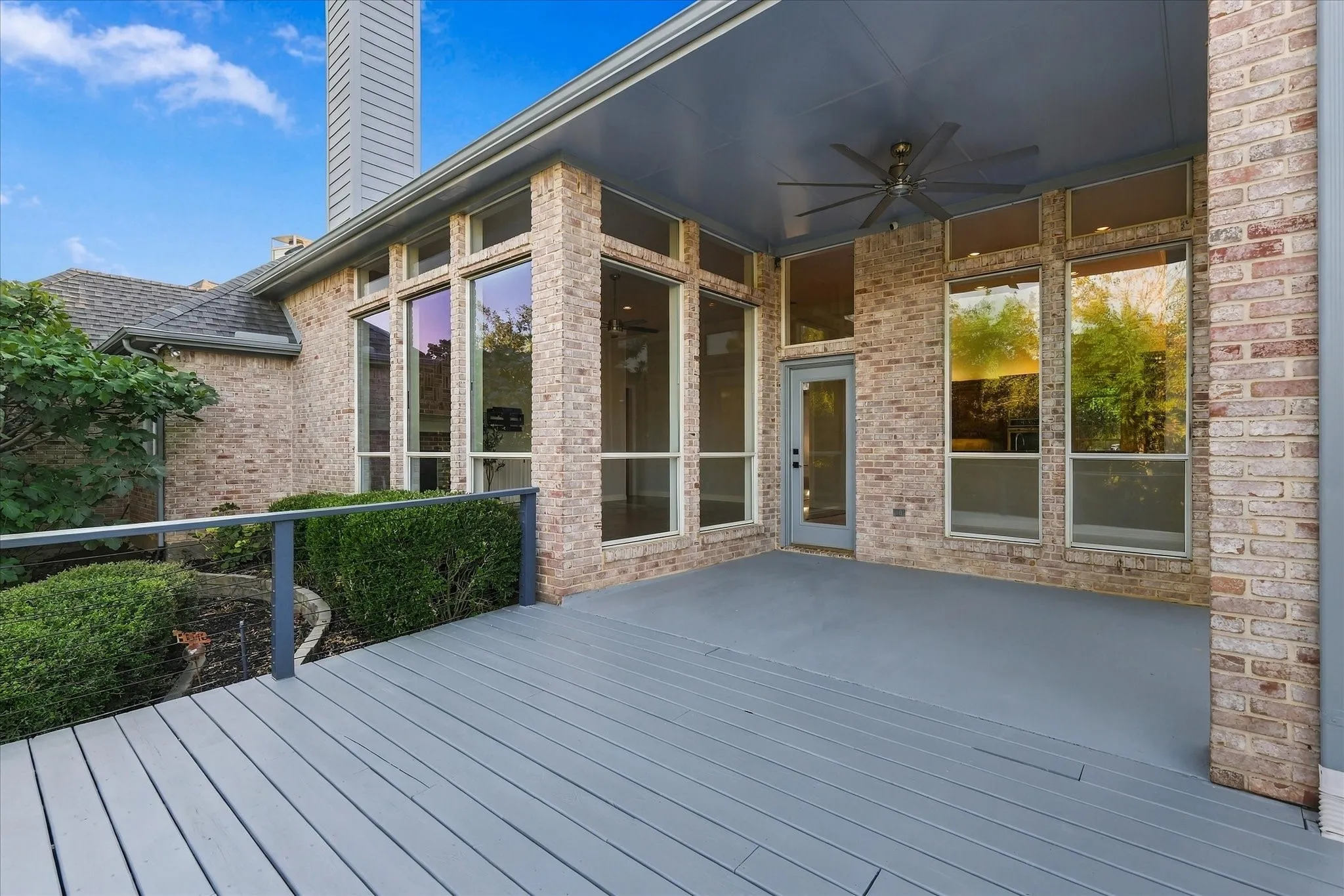 Expansive outdoor decking, brick exterior, large picture windows, covered patio, and ceiling fan