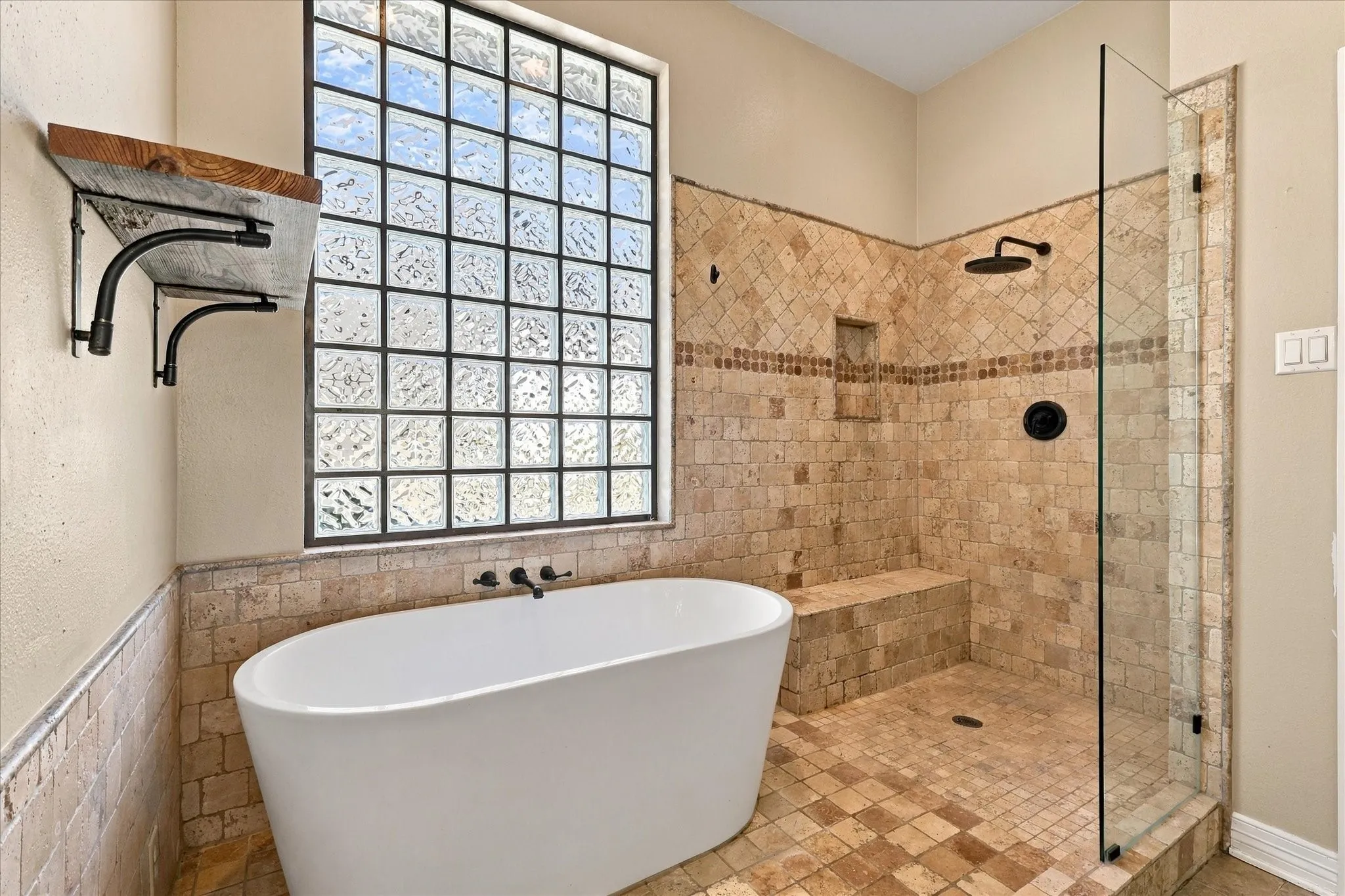 Freestanding soaking tub with matte black fixtures, glass block window, and separate shower with tiled walls, built-in bench, and black rainfall showerhead