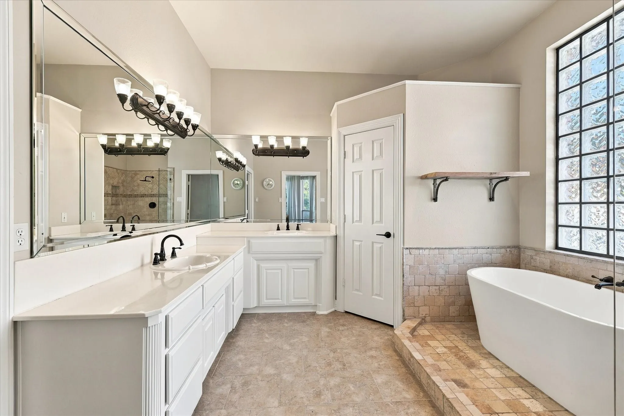 Dual vanity with white cabinetry and integrated sinks, a freestanding tub, tiled bathing area, large glass block window, and extensive wall-mounted mirrors