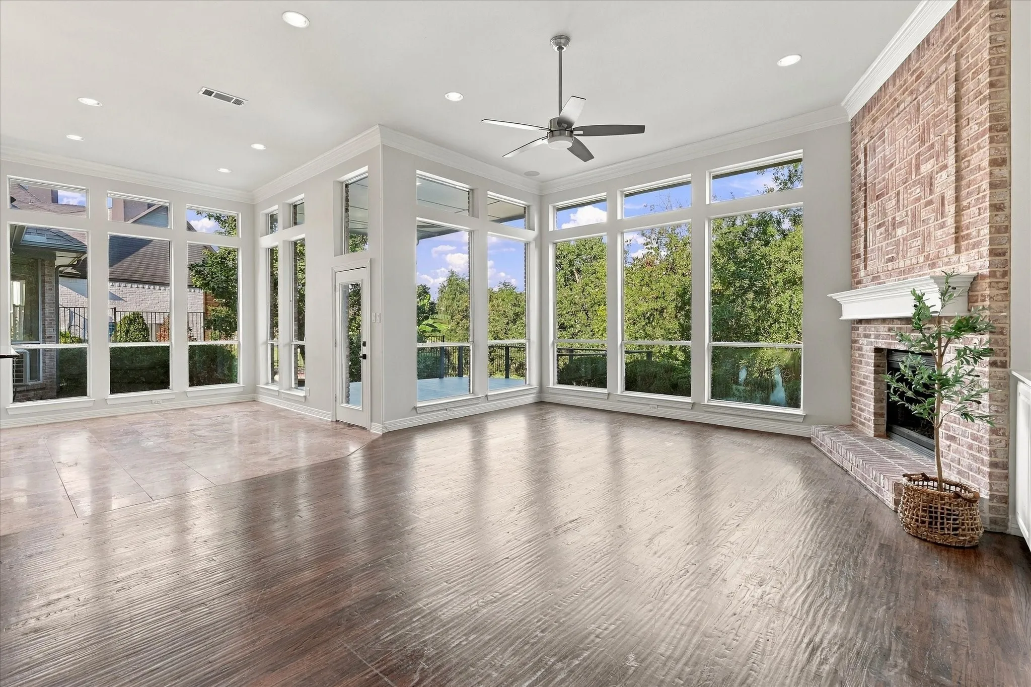 Expansive room featuring multi-pane windows, a brick-surround fireplace with a white mantel, and wood-finish flooring