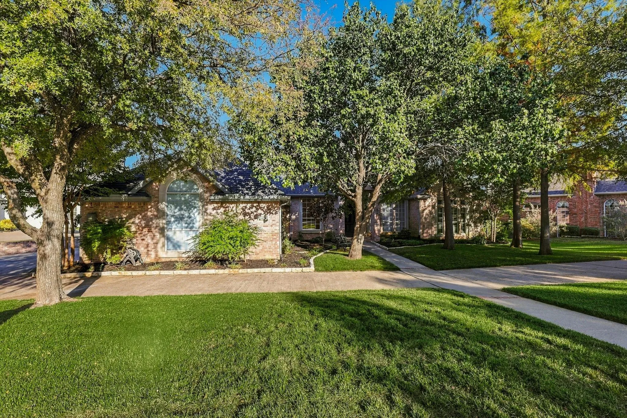 Brick exterior with an arched window, mature trees, and a concrete pathway