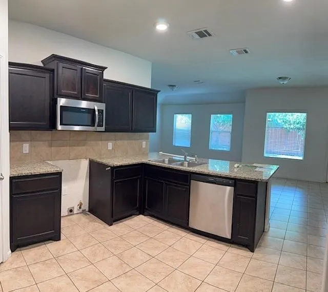 Spacious kitchen featuring dark wood cabinetry, light-toned tiled flooring, a stainless steel microwave, and a double basin sink