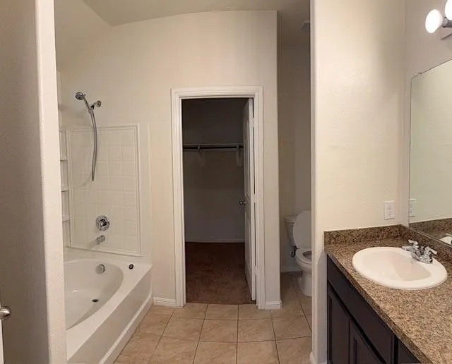 Bathroom featuring a tiled floor, a vanity with a countertop and undermount sink, a large mirror, a separate tub and shower combination with white subway tile surround, and a toilet