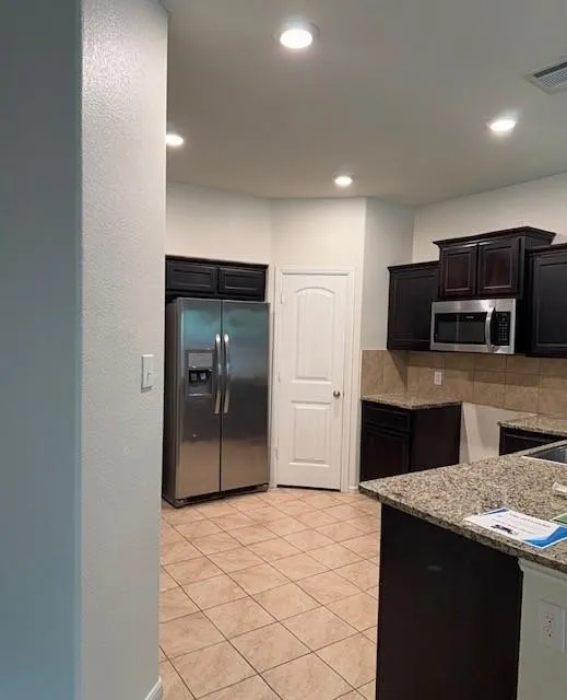 Kitchen featuring dark wood-finish cabinetry, stainless steel appliances, granite-style countertops, and a tiled backsplash