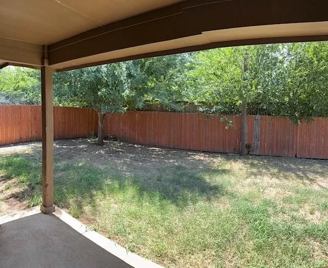 Covered patio with concrete flooring overlooking a private backyard featuring a wood privacy fence, mature trees, and natural landscaping