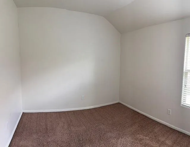 Carpeted room with a vaulted ceiling, white walls, and a window with blinds