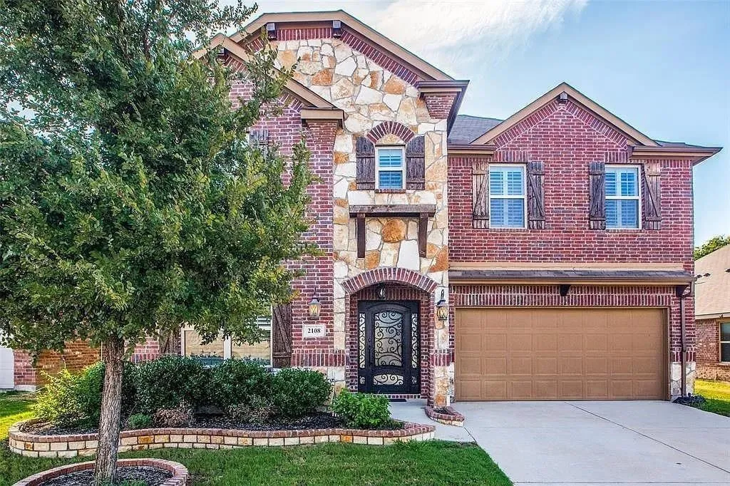 Brick and stone facade featuring decorative shutters, a single-car garage, and a wrought iron front door