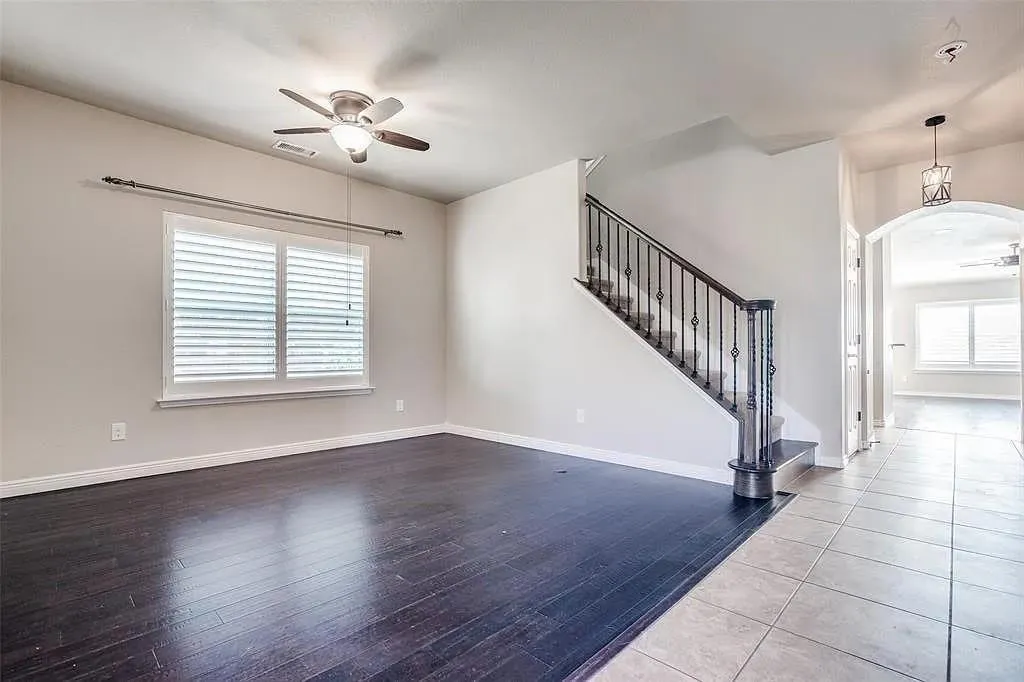 Wood-finish flooring, staircase with wrought iron balusters, ceiling fan, window with horizontal blinds, and tiled entryway
