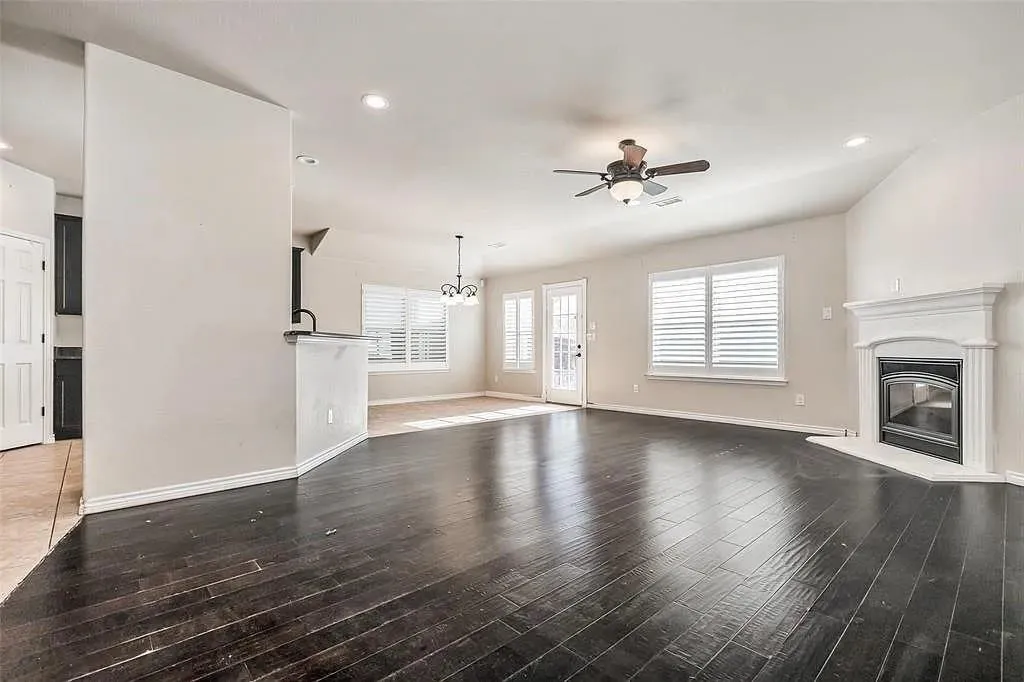 Dark wood-finish flooring, a white mantel fireplace, a ceiling fan with integrated lighting, recessed lighting, and white window shutters