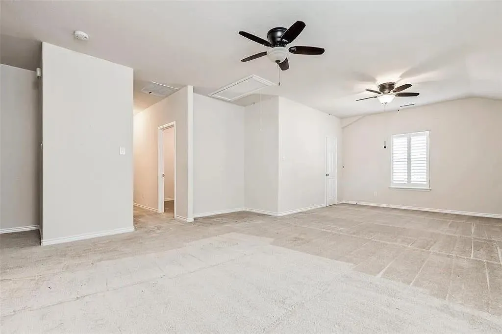Spacious room with sloped ceilings, two ceiling fans with integrated lighting, and a window with white louvered shutters