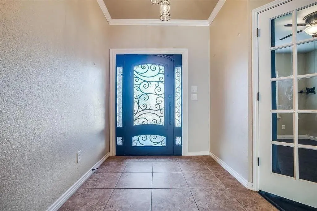 Tile flooring, crown molding, decorative glass entry door, and a glass-paneled interior door