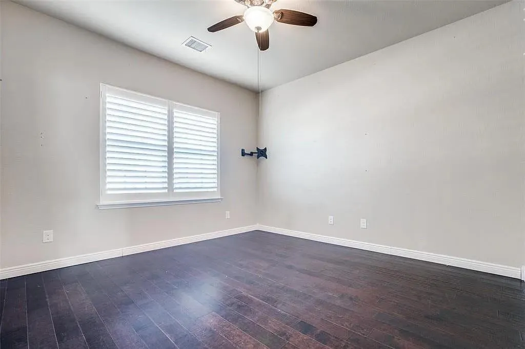 Dark wood-finish flooring, white wall paint, window with white louvered shutters, and a ceiling fan with integrated lighting