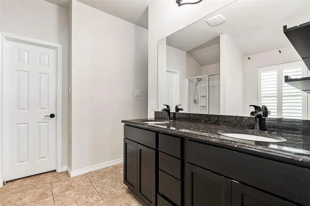Dual vanity with dark cabinetry, granite countertop, undermount sinks, and matte black fixtures