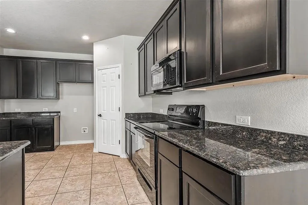 Kitchen featuring dark cabinetry, dark speckled countertops, tile flooring, and integrated stainless steel​​‌​​​​‌​​‌‌​‌‌​​​‌‌​‌​‌​‌​​​‌​​ appliances