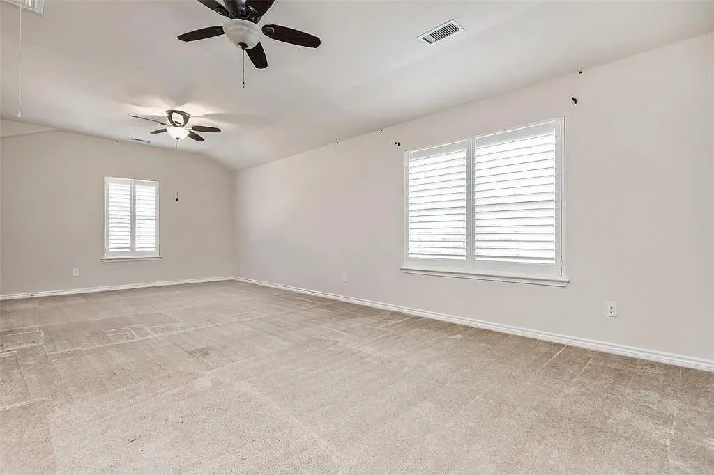 Spacious room featuring vaulted ceilings, two ceiling fans, and two windows with white plantation shutters