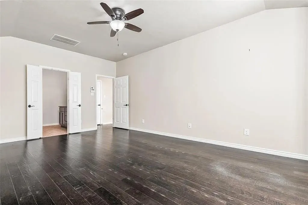 Dark wood-finish flooring, vaulted ceiling, and a ceiling fan with integrated lighting