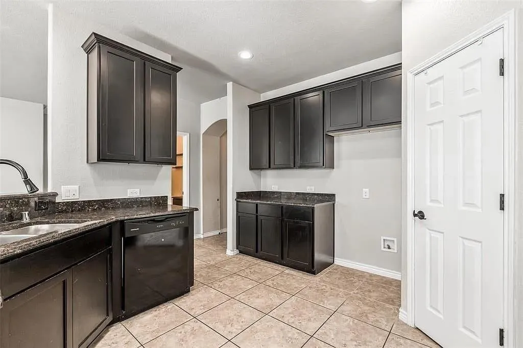 Kitchen featuring dark wood-finish cabinetry, dark countertops, a stainless steel sink with a gooseneck faucet, and a black dishwasher